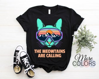 Könnte beinhalten: Schwarzes T-Shirt mit einem Grafikdruck eines Katers mit Skibrille und dem Text "The Meowtains Are Calling".