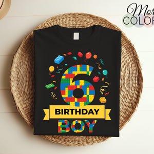 Könnte beinhalten: Schwarzes T-Shirt mit einer bunten Zahl Sechs aus Spielzeugbausteinen. Die Zahl ist von Konfetti und Luftballons umgeben. Der Text "Birthday Boy" ist unter der Zahl aufgedruckt.