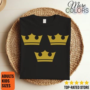 May include: Black t-shirt with three gold crowns. The garment is presented on a woven basket. Text on the image includes "More Colors", "Adults Kids Sizes", and "Top-Rated Store".