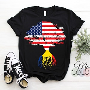 K&ouml;nnte beinhalten: Schwarzes T-Shirt mit einem Baumdesign. Die Bl&auml;tter des Baumes sind die amerikanische Flagge und die Wurzeln sind die ukrainische Flagge. "Mehr Farben" steht in wei&szlig;er Schrift mit einem kleinen Kreis von Farbmustern darunter.