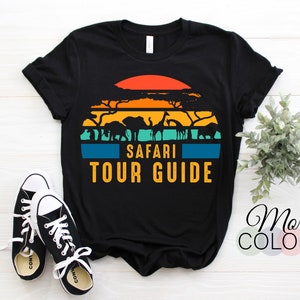 Peut inclure: T-shirt noir avec un graphique de coucher de soleil rétro représentant des silhouettes d'animaux africains et le texte "Safari Tour Guide".