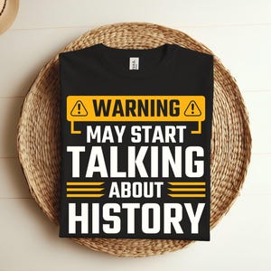 Puede incluir: Camiseta negra con una señal de advertencia amarilla que dice "Advertencia Puede Empezar a Hablar de Historia".