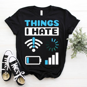 May include: Black t-shirt with the text "THINGS I HATE" in blue and white. The shirt features graphics of a wifi signal, a loading symbol, a battery, and a signal bar. Black and white trainers are in the foreground.