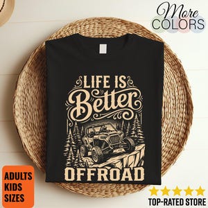 Op de afbeelding: Een zwart t-shirt met een beige grafische print van een terreinwagen die op een rotsachtige klif tussen dennenbomen rijdt. De tekst "LIFE IS BETTER OFFROAD" staat in een gestileerd lettertype in het midden op de voorzijde van het shirt.