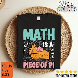Puede incluir: Camiseta negra con la frase "MATH IS A PIECE OF PI" en turquesa y rosa. El diseño incluye una porción de tarta con un toque de crema batida rosa y símbolos matemáticos. La camiseta se muestra sobre una superficie tejida.