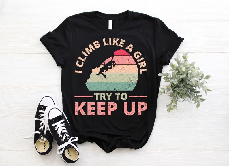 May include: Black t-shirt with a vintage-style graphic of a person rock climbing. The graphic says "I climb like a girl - try to keep up".