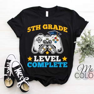 May include: Black t-shirt with a yellow and blue graphic of a video game controller with a graduation cap on top. The text "5th Grade Level Complete" is printed on the shirt.