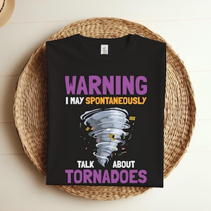 Op de afbeelding: Zwart T-shirt met een paarse en gele afbeelding van een tornado met de tekst "WARNING I MAY SPONTANEOUSLY TALK ABOUT TORNADOES".