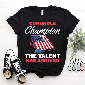 May include: Black t-shirt with a white American flag cornhole board graphic and the text "Cornhole Champion The Talent Has Arrived".