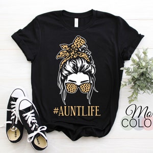 May include: Black t-shirt with a graphic of a woman with a messy bun and leopard print headband and sunglasses. The text "#AUNTLIFE" is below the graphic.