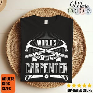 Könnte beinhalten: Schwarzes T-Shirt mit weißer Grafik, die "WORLD'S MOST AWESOME CARPENTER" lautet. Das Design umfasst gekreuzte Hämmer und Sägen. Das Shirt wird auf einem geflochtenen Korb präsentiert. Text auf dem Bild zeigt, dass Größen für Erwachsene und Kinder verfügbar sind.