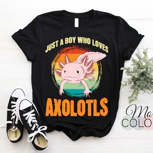 Könnte beinhalten: Schwarzes T-Shirt mit einem farbenfrohen Axolotl-Motiv und dem Text "JUST A BOY WHO LOVES AXOLOTLS" im Retro-Stil. Ein Paar schwarz-weiße Turnschuhe sind im Vordergrund zu sehen.