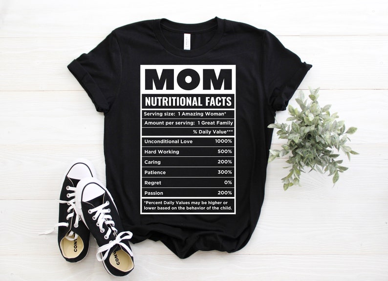 May include: Black t-shirt with a white graphic that reads "MOM NUTRITIONAL FACTS." The graphic lists values for Unconditional Love, Hard Working, Caring, Patience, Regret, and Passion. Black and white sneakers are in the foreground.