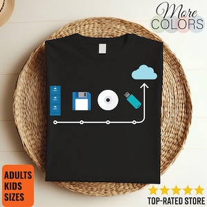 May include: Black t-shirt with a graphic depicting the evolution of data storage: a file cabinet, floppy disk, CD, and USB drive leading to a cloud icon. The shirt has the text "More Colors" and "Adults Kids Sizes".