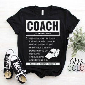 Könnte beinhalten: Schwarzes T-Shirt mit dem Wort "COACH" in einem weißen Rechteck, zusammen mit einer Definition und einer Pfeifengrafik. Die Definition beschreibt eine leidenschaftliche Person, die das Potenzial freisetzt. Schwarz-weiße Turnschuhe sind unten.