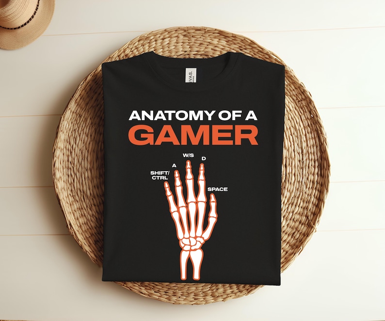 K&ouml;nnte beinhalten: Schwarzes T-Shirt mit dem Text "Anatomy of a Gamer" in Wei&szlig; und einer Skeletthand mit den Tasten "W, S, A, D, Shift, Ctrl, Space" in Orange.