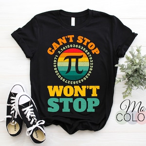 May include: Black t-shirt featuring the text "CAN'T STOP WON'T STOP" in orange and green, with a Pi symbol and digits. A pair of black and white trainers are in the foreground.