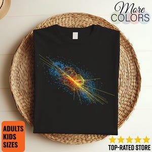 May include: A black t-shirt featuring a vibrant graphic print of a particle physics collision event. The design displays intricate yellow and red circular patterns surrounded by a cloud of blue dots, set against the solid black fabric of the shirt.