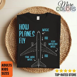 Puede incluir: Camiseta negra con un diagrama de un avión y el texto "HOW PLANES FLY" en azul claro. El diagrama incluye etiquetas como "MAGIC" y "AIR". La camiseta también tiene el texto "ADULTS KIDS SIZES" en un cuadro naranja.