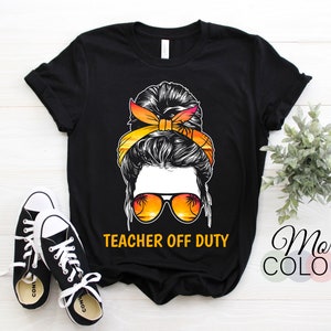 Könnte beinhalten: Schwarzes T-Shirt mit einer Grafik einer Frau mit Sonnenbrille und einem Sonnenuntergangsdesign. Der Text "TEACHER OFF DUTY" ist in Gelb gedruckt. Schwarz-weiße Turnschuhe sind im Vordergrund. Die Worte "More Colors" sind im Hintergrund.