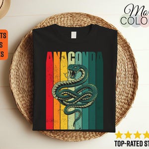 Puede incluir: Una camiseta negra con un gráfico de estilo retro de una serpiente verde con la palabra "ANACONDA" en letras amarillas arriba.