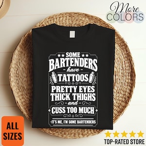 May include: A black t-shirt featuring white text that reads: SOME BARTENDERS HAVE TATTOOS, PRETTY EYES, THICK THIGHS AND CUSS TOO MUCH, IT'S ME, I'M SOME BARTENDERS. The design includes two small cocktail shaker icons and decorative border elements.