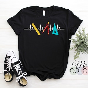 May include: Black t-shirt with a white heartbeat line design incorporating a ruler, compass, and triangle. The shirt has rolled-up sleeves and is paired with black and white sneakers. The words "More Colors" are visible in the bottom right corner.