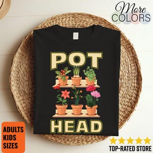 May include: Black t-shirt with the words "POT HEAD" in a light green font. The design features a shelf with potted plants and flowers. The shirt is displayed on a woven surface. The shirt is available in adult and kids sizes.
