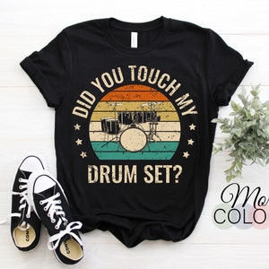 以下が含まれることがあります： ドラムセットのヴィンテージスタイルのグラフィックと「Did you touch my drum set?」というテキストが書かれた黒いTシャツ