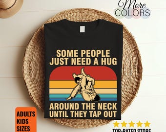 May include: Black t-shirt with a retro design featuring a martial arts illustration and the text "SOME PEOPLE JUST NEED A HUG AROUND THE NECK UNTIL THEY TAP OUT." The shirt also has the words "ADULTS KIDS SIZES".