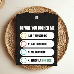 May include: Black t-shirt with white text that reads "BEFORE YOU BOTHER ME" and a checklist with four items: "1. IS IT PLUGGED IN?", "2. IS IT TURNED ON?", "3. ARE YOU SURE?", "4. SERIOUSLY, GO CHECK".
