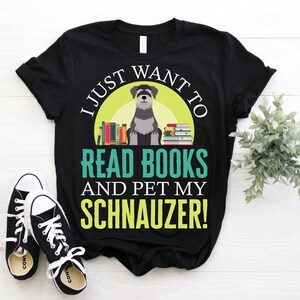 May include: Black t-shirt with the text "I JUST WANT TO READ BOOKS AND PET MY SCHNAUZER!" featuring a Schnauzer dog illustration, books, and a green and yellow background. Black and white sneakers are in the foreground.