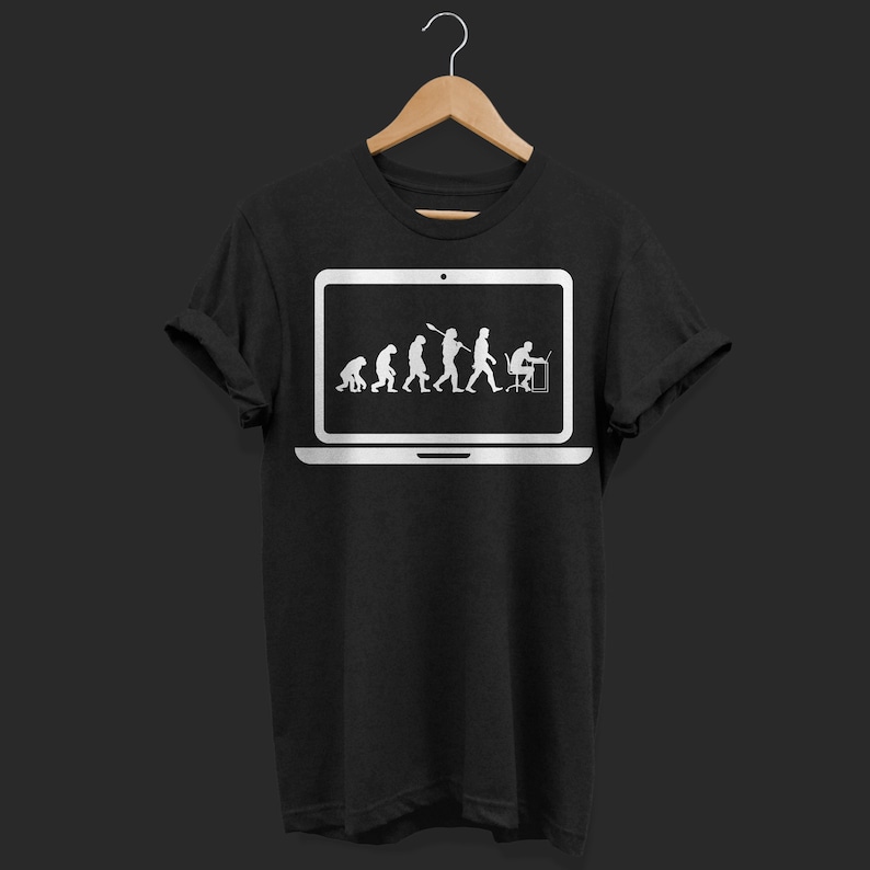 May include: Black t-shirt with a white graphic depicting human evolution within a laptop screen. The design shows the progression from early hominids to a person using a computer. The t-shirt is hanging on a wooden hanger.