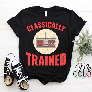 May include: Black t-shirt with the text "Classically Trained" in red and white. A vintage-style video game controller is in a circle above the text.