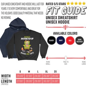 May include: A black unisex sweatshirt with the text "Easily Distracted by Books and Cats" and a graphic of a cat reading a book in a chair. The size chart shows the width and length in inches for sizes S, M, L, XL, and 2X. The available colors are black, navy, red, and dark heather.