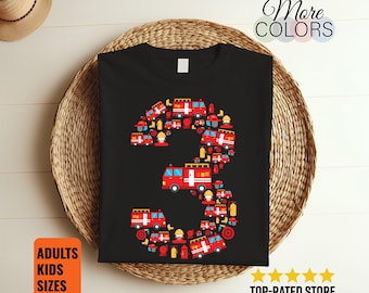 Puede incluir: Camiseta negra con el número "3" formado por camiones de bomberos rojos, cascos y otros gráficos relacionados con los bomberos. La camiseta también muestra las palabras "More Colors" y "Adults Kids Sizes".