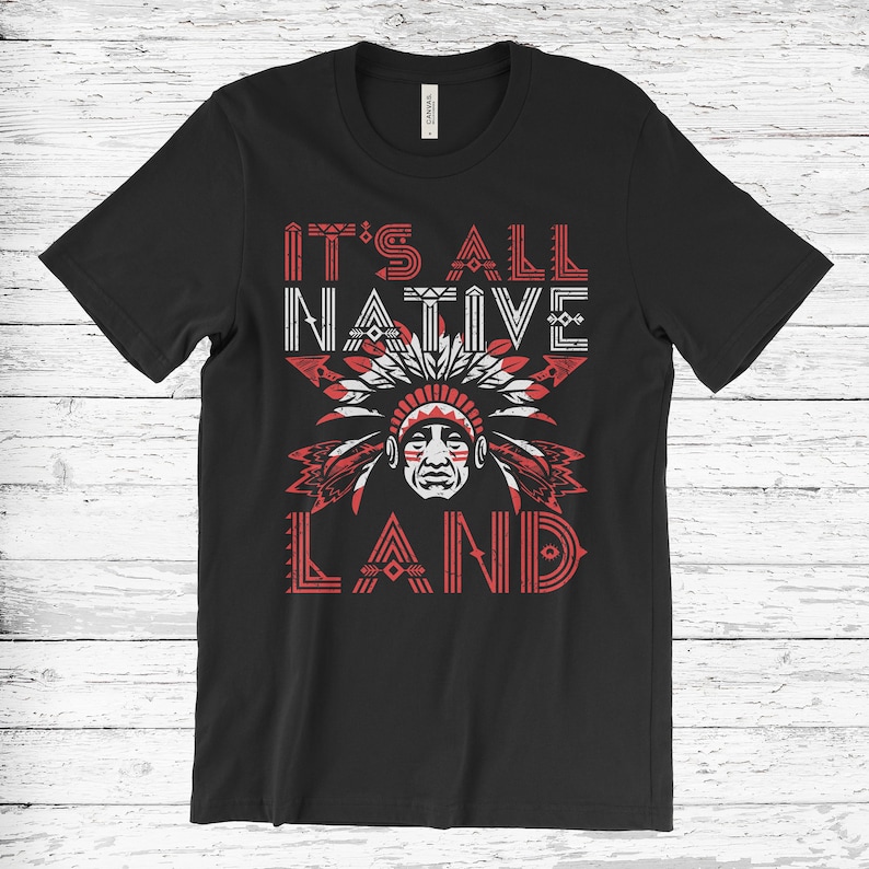 May include: Black t-shirt with a red and white graphic design. The graphic features a Native American headdress and the text "It's All Native Land".