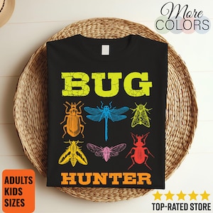 Peut inclure: T-shirt noir avec un motif graphique coloré représentant le mot "BUG" en jaune et le mot "HUNTER" en orange. Le motif comprend des illustrations de divers insectes en orange, bleu, jaune, rose et rouge. Le t-shirt porte également les mentions "More Colors", "Adults Kids Sizes" et "Top-Rated Store".
