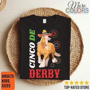 Peut inclure: T-shirt noir avec un cheval de dessin animé portant un sombrero, avec le texte "Cinco de Derby" en vert et rouge. Le t-shirt porte également le texte "Adultes Tailles Enfants" et "Plus de couleurs".