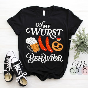 Può includere: Maglietta nera con testo bianco che recita "On My Wurst Behavior". Il design include una birra, pretzel e salsicce.