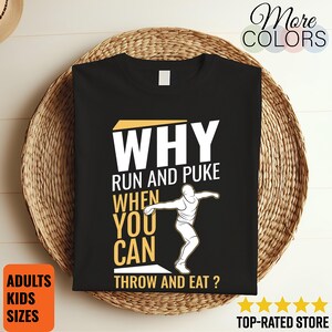 May include: Black t-shirt with the text "WHY RUN AND PUKE WHEN YOU CAN THROW AND EAT ?" in white and yellow. The shirt features a graphic of a person throwing a discus. The shirt is displayed on a woven basket.