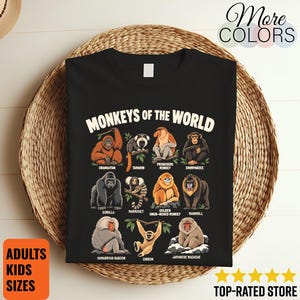 May include: A black t-shirt featuring a graphic print titled MONKEYS OF THE WORLD with illustrations and labels for an orangutan, tamarin, proboscis monkey, chimpanzee, gorilla, marmoset, golden snub-nosed monkey, mandrill, hamadryas baboon, gibbon, and Japanese macaque.