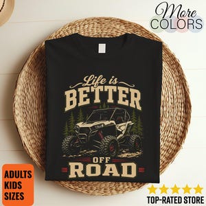 Könnte beinhalten: Ein schwarzes T-Shirt mit einem Grafikdruck eines Geländewagens vor grünen Kiefern. Der Text lautet Life is BETTER OFF ROAD in beigen und roten Buchstaben. Das Design enthält eine stilisierte Illustration eines vierrädrigen Fahrzeugs.