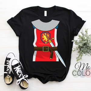 May include: Black t-shirt with a graphic of a knight in armor. The knight is wearing a red tunic with a gold belt and a sword. The knight's shield has a lion on it.