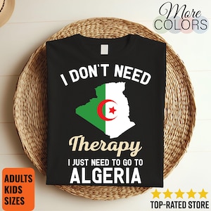 Peut inclure: T-shirt noir avec le texte "I DON'T NEED Therapy I JUST NEED TO GO TO ALGERIA." Le t-shirt présente un graphique du drapeau algérien. Le t-shirt est présenté sur un panier en osier. Les mots "ADULTS KIDS SIZES" sont dans un carré orange.