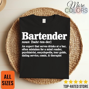May include: A black t-shirt featuring white text that defines the word Bartender as an expert that serves drinks at a bar, often mistaken for a mind reader, psychiatrist, encyclopedia, tour guide, dating service, comic, and therapist.