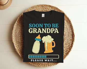 May include: Black t-shirt with the text "Soon to be Grandpa" in blue and yellow.  A baby bottle and a beer mug are pictured below the text. A progress bar with the text "Please wait..." is at the bottom of the shirt.