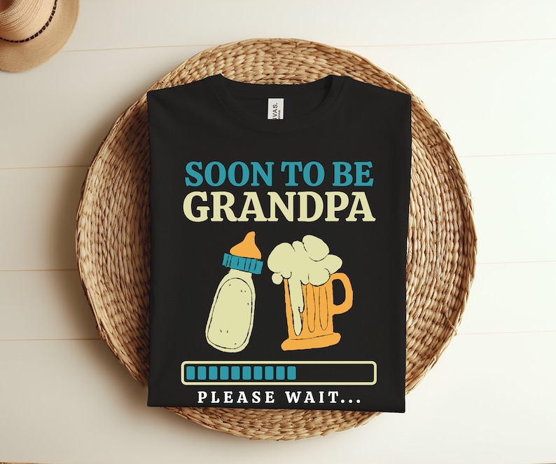 May include: Black t-shirt with the text "Soon to be Grandpa" in blue and yellow.  A baby bottle and a beer mug are pictured below the text. A progress bar with the text "Please wait..." is at the bottom of the shirt.