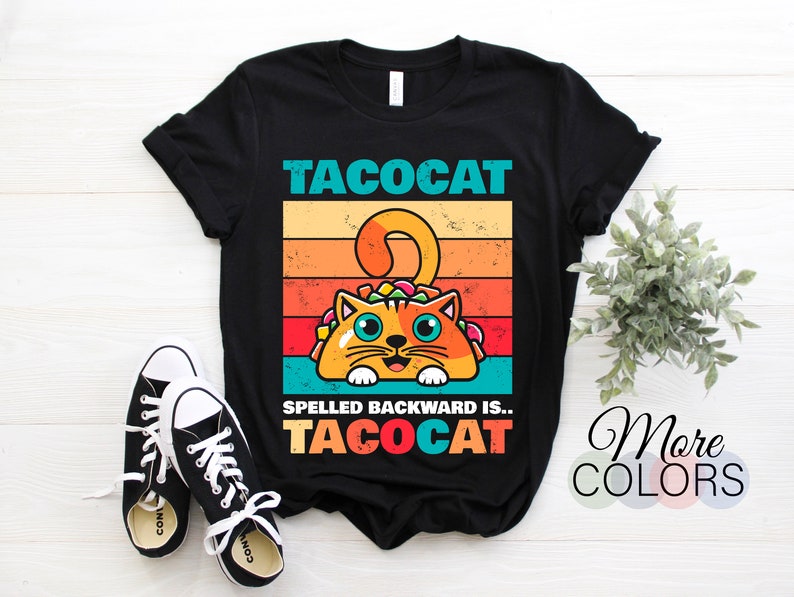 May include: Black t-shirt with a retro-style graphic of a cat holding a taco. The text "Tacocat" is above the cat and the text "Spelled backward is... Tacocat" is below the cat.