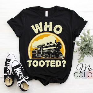 May include: Black t-shirt with a yellow circle and a cartoon train with the text "Who Tooted?" printed on it.